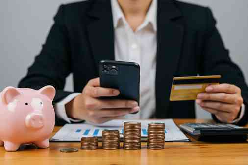 Mann mit Smartphone, Bankomatkarte, Sparschwein und Münzen